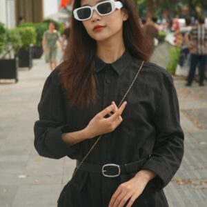 Stylish Asian woman in urban setting wearing black fashion and sunglasses.
