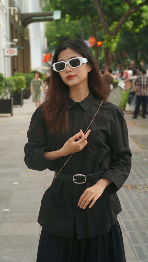 Stylish Asian woman in urban setting wearing black fashion and sunglasses.