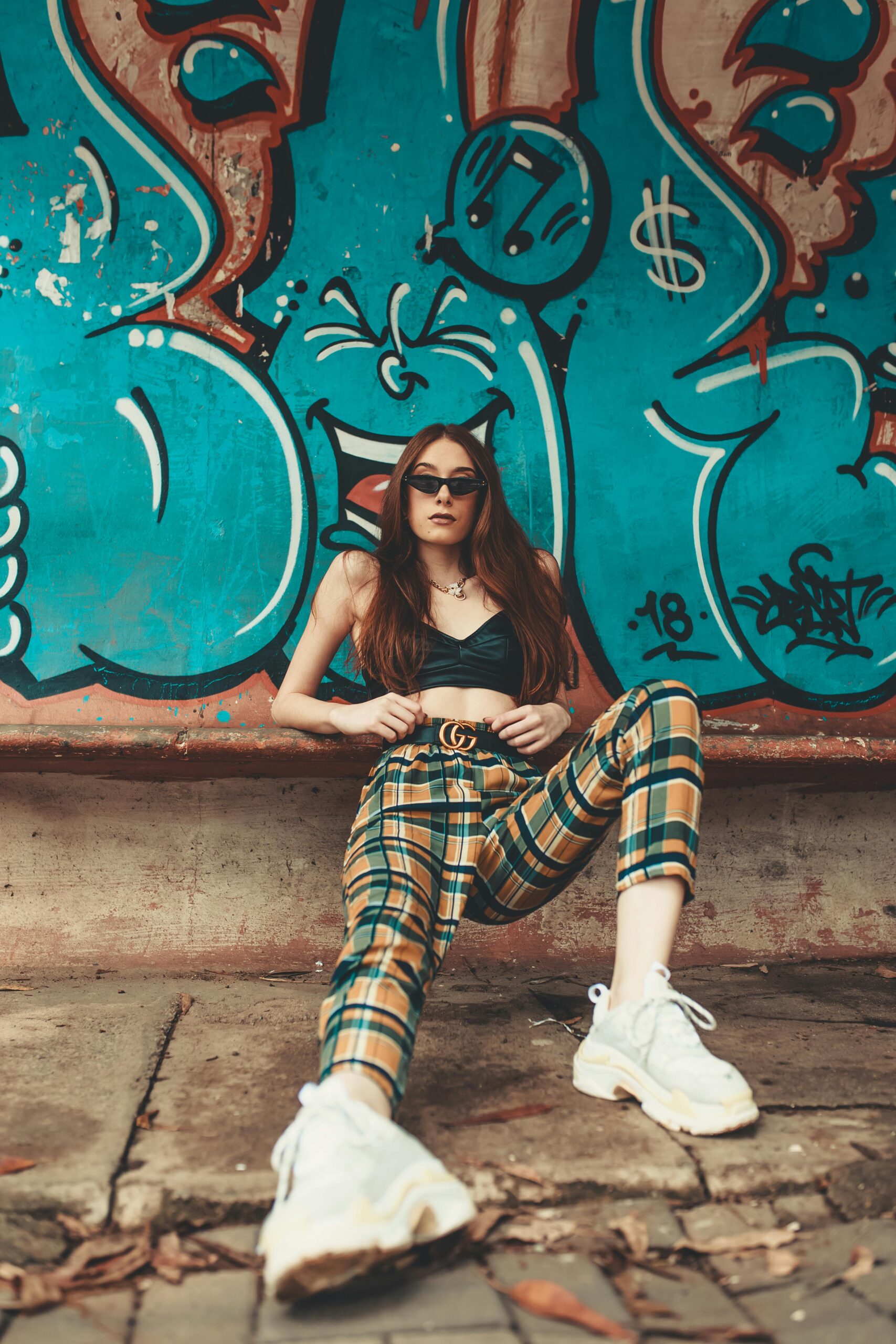 Trendy woman in plaid pants poses confidently against vibrant graffiti wall.