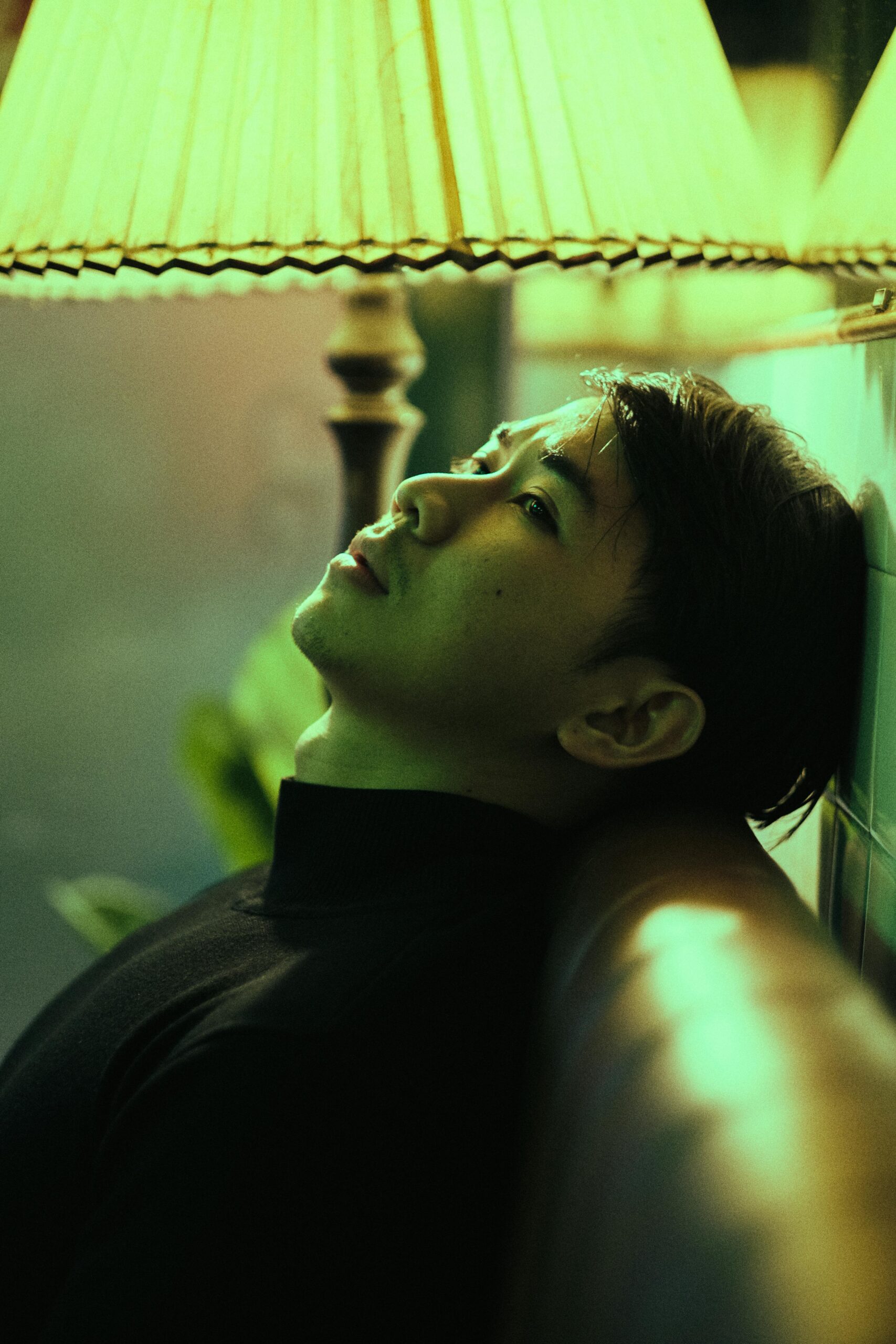 Side view of thoughtful Asian man sitting on leather couch near floor lamp