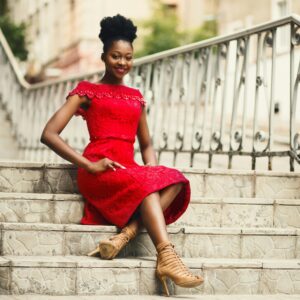 Young woman in a red lace dress sitting on outdoor steps, smiling and posing.